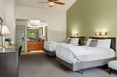 A cozy hotel room featuring two beds, a desk, and a bathroom area with modern decor and warm lighting.